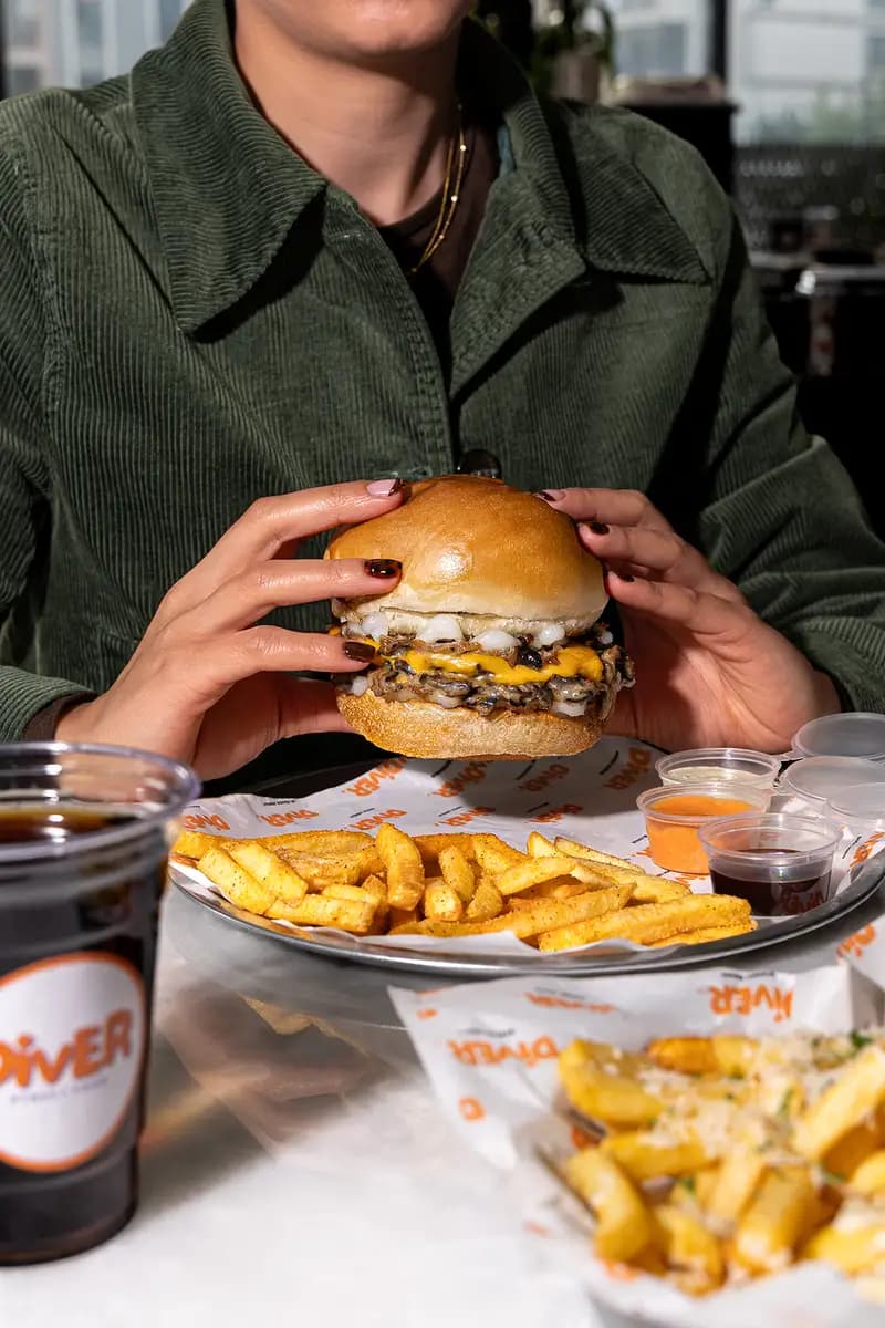 İki elle tutulan double cheese burger ve yanında patates tepsisi.