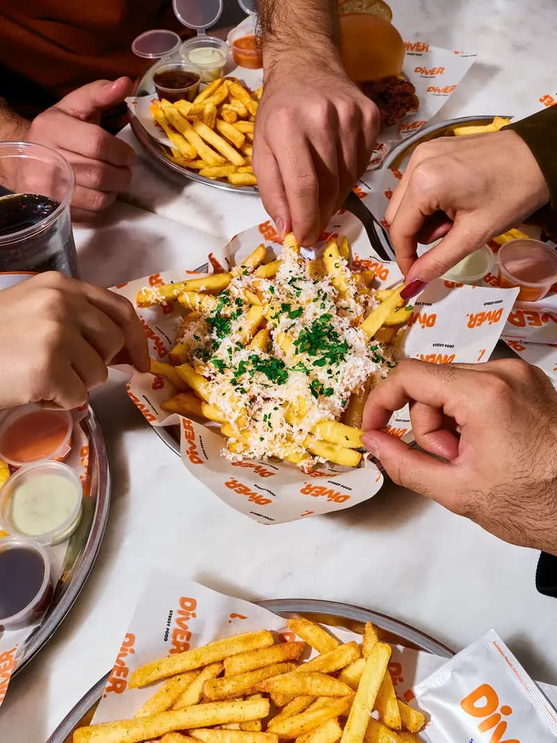 Ortada paylaşılan, sos ve yeşillikle kaplı loaded fries tabağı.